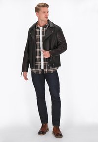 Jachetă din piele neagră cu rever larg, asortată cu o cămașă în carouri maro și alb, blugi de denim închis și cizme maro cu șireturi.