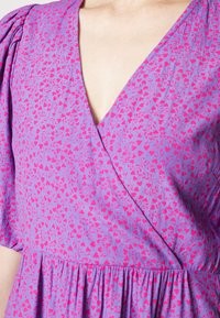 Vestido envolvente púrpura con estampado de corazones rojos y enredaderas, con mangas cortas abullonadas y cintura fruncida, que muestra el escote y la parte superior del torso.
