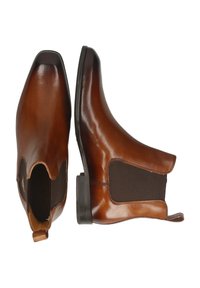 Botas de tobillo de cuero marrón con paneles laterales elásticos, punta afilada y una textura suave. Incluyen una tira en el talón para facilitar su colocación.