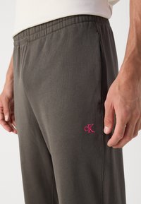 Huisgrijze sweatpants met een elastische tailleband en zijzakken, met een klein roze geborduurd logo op de linkerdij.