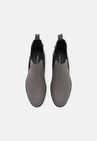 Un paio di stivali Chelsea in suede grigio con pannelli elastici neri ai lati e linguette per il pull, visti dall'alto su uno sfondo bianco.