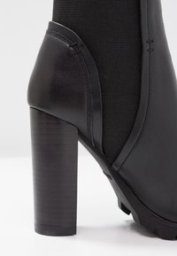 Bottine noire avec une tige en cuir texturé, un panneau élastique lisse et un talon épais à rayures pour la stabilité.