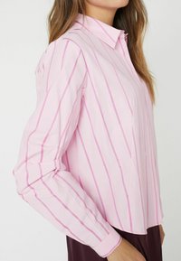 Camicia button-up rosa chiaro con strisce verticali bianche e rosa, maniche lunghe, colletto e un taglio rilassato. Tessuto texturizzato.