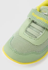 Πράσινο πλεκτό αθλητικό παπούτσι με κίτρινες λεπτομέρειες και λουράκι Velcro. Λείες συνθετικές επικαλύψεις και υφασμένο πλέγμα που βελτιώνει την αναπνοή.