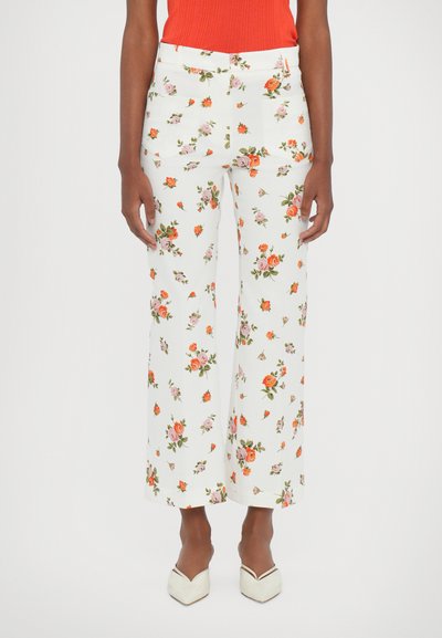 White floral trousers featuring a multicolored rose pattern. Flared design, mid-rise waist, and two front pockets. Paired with a red ribbed top.