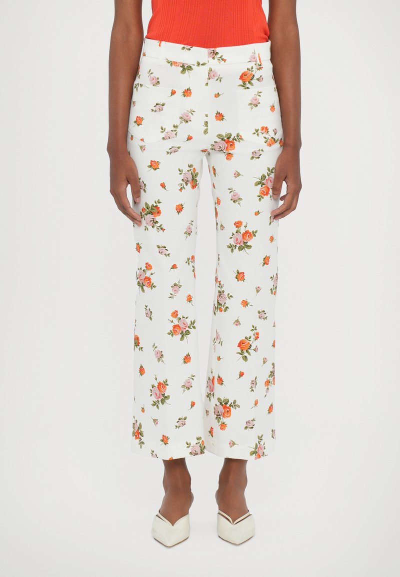 White floral trousers featuring a multicolored rose pattern. Flared design, mid-rise waist, and two front pockets. Paired with a red ribbed top.