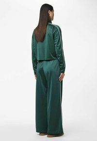 Grøn satin træningstøj med en cropped top og vide bukser, der har hvide sidelister. Glat tekstur med en blank overflade.