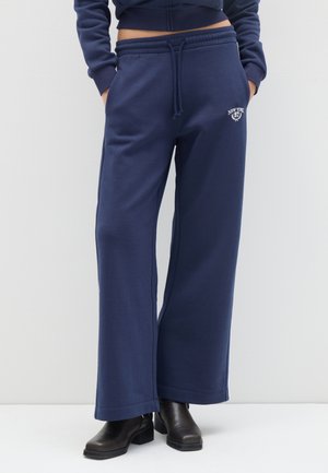 Pantalones de chándal de pernera ancha en color azul marino, confeccionados en un tejido suave, con una cintura elástica y cordón de ajuste, y un logo bordado que dice "New York 97".