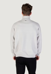 Lichtgrijze coltrui met een losse pasvorm en geribbelde manchetten. Heeft een minimalistisch ontwerp en een soepele textuur. Zwarte broek zichtbaar onderaan.