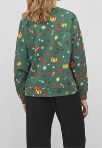 Grön sweatshirt med ett festligt mönster av presenter, renar, järnek, polkagrisar och snöflingor i rött, gult och vitt. Mjukt tyg, avslappnad passform.