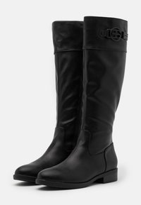 Botas de cuero negras hasta la rodilla con una textura suave, cremallera lateral y una hebilla decorativa en el puño. Punta redondeada y tacón bajo tipo bloque.