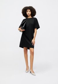 Black short-sleeve dress with a relaxed fit, featuring a round neckline and smooth texture, paired with a structured black handbag and light gray heels.