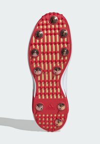 Red and white athletic shoe sole with a textured pattern, featuring gold-colored studs for traction, and a rubberized grip.