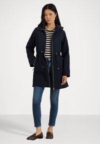 Navy gevoerd jasje met capuchon, trekkoord in de taille, rits sluiting aan de voorkant en twee zijzakken; gecombineerd met gestreepte top en denim.