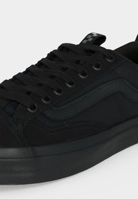 Μαύρο χαμηλό sneaker με κορδόνια μπροστά, ανάγλυφη πλευρική ρίγα και παχιά λαστιχένια σόλα σε ουδέτερο φόντο.