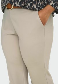 Bež hlače od glatkog tkanja, s bočnim džepovima, ravnim krojem nogavica i suptilnim detaljima šavova.