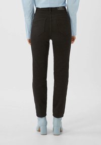 Vaqueros de mezclilla negra con cintura alta, pierna recta y bolsillos traseros, combinados con botas de tobillo azul claro con tacón grueso.