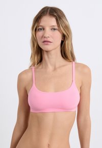 Bralette rosa chiaro con sottili spalline regolabili, texture liscia e scollatura arrotondata. Nessun chiusura o decorazione visibile.