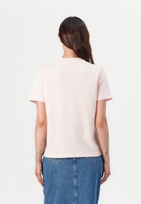 Lys rosa bomulls t-skjorte med korte ermer og rund hals, sett fra baksiden, parret med et denim skjørt. Enkel og uornamentert design.