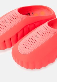 Φωτεινά ροζ ξύλινα παπούτσια με διάτρητο σχέδιο, λεία υφή και παχύ ραβδωτό πάτο. Διαθέτουν διακριτικό λογότυπο στο πάνω μέρος. Ελαφρύ υλικό.