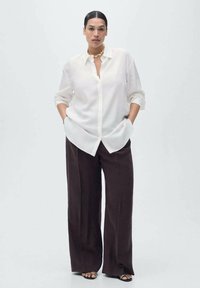 White button-up shirt with a relaxed fit and rolled sleeves, paired with dark brown wide-leg trousers. Simple design with no patterns.