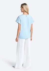 Haut bleu clair à manches courtes avec un col rond et des détails de boutons au dos, associé à un pantalon large blanc et décontracté. Tissu doux et texturé.