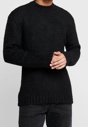 Zwarte gebreide trui met een geribbelde textuur, ronde halslijn en lange mouwen. Heeft een iets langere achterkant en gedetailleerde boorden.