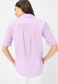 Lichtpaarse shirt met korte mouwen, voorzien van een kraag, geplooide achterkant en opgerolde manchetten, gemaakt van een zachte, lichte stof.