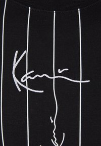 Black fabric with white vertical stripes and embroidered signature "Kani" on the front. Smooth texture and minimalist design.