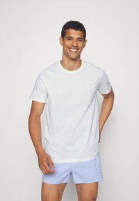 White cotton t-shirt with a round neckline and short sleeves, paired with blue gingham-patterned shorts. Smooth texture, casual design.