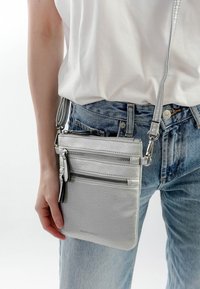 Stříbrná kožená crossbody taška s několika zipovými kapsami, texturovaným povrchem, štíhlým tvarem a nastavitelným popruhem.