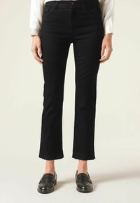 Svarta denimjeans med figurnära passform, kort längd, fransad fåll och klassisk femfickdesign, tillsammans med svarta loafers.