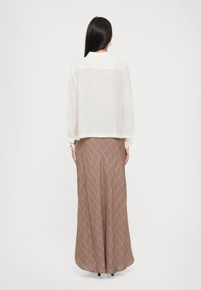 Sheer white blouse with gathered sleeves and ties, paired with a long brown-patterned skirt featuring diagonal lines in red and beige.