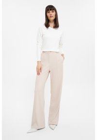 Leichte beige Hosen mit einem weit geschnittenen Design, ausgestattet mit seitlichen Taschen und einer glatten Textur. Kombiniert mit einem taillierten weißen Langarmoberteil.