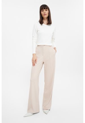 Pantalones beige ligeros con un diseño de pierna ancha, que cuentan con bolsillos laterales y una textura suave. Combinados con una camiseta blanca de manga larga ajustada.