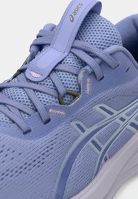 Hele lilla sportkinga võrgusülemsusega, siledate sünteetiliste detailide ja tekstureeritud tallaga. Varustatud paelte ja brändi logoga.