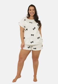 Białe bawełniane piżamy z czarnymi wzorami w kokardki, z luźną górą i szortami wykończonymi falbankami. Gładka tekstura i swobodny design.