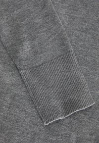 Grau gestrickter Stoff mit einem gerippten Bündchen-Detail. Strukturelle Oberfläche, weiche Haptik und subtile Farbvariationen. Nahaufnahme des Ärmels.