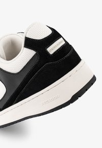 Black and white sneaker featuring a mix of leather and mesh, with a textured sole, rounded toe, and branded accents on the heel.