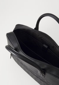 Black leather bag with textured surface, zip closure, and a smooth handle. Interior features a black fabric lining and a slip pocket.
