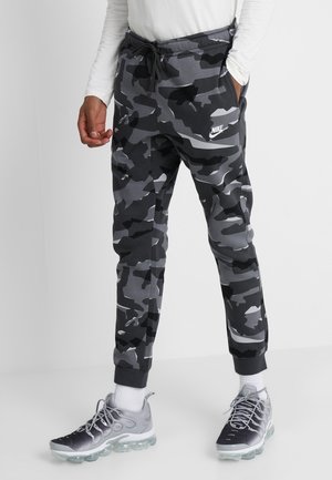 Grijze camouflage joggingsbroek met een elastische tailleband, zijzakken en een wit logo op het linkerbeen. Afgerond met grijze sportschoenen.