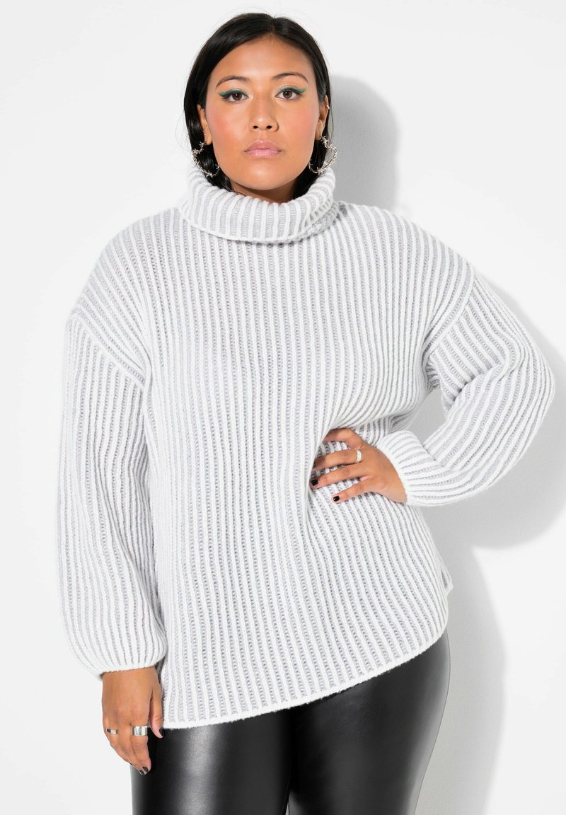 Helles graues, geripptes Strickrollkragensweatshirt mit langen Ärmeln und asymmetrischem Saum; getragen mit schwarzen Leggings. Texturiertes Material sichtbar.