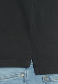 Svart teksturert skjorte med sideslit, kombinert med lyseblå jeans med metallknapper. Stoffet ser ut til å være pustende og vevd.