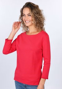 Rot- und pinkgestreifter Langarmoberteil mit Rundhalsausschnitt und gewellten Kanten, aus weichem Stoff gefertigt, kombiniert mit blauen Jeans.