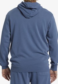 Felpa blu in cotone con vestibilità comoda, polsini e orlo a coste. Presenta una grande tasca posteriore e un cappuccio con cordoncino. Texture morbida.