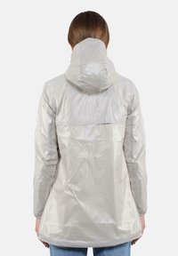 Giacca impermeabile grigia chiara con cappuccio, texture liscia, polsini elasticizzati e orlo posteriore leggermente più lungo per una migliore copertura.