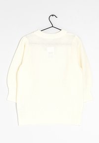 Suéter de punto ligero de color crema con un corte holgado, puños acanalados y un patrón de puntada abierta, colgado de un gancho negro.