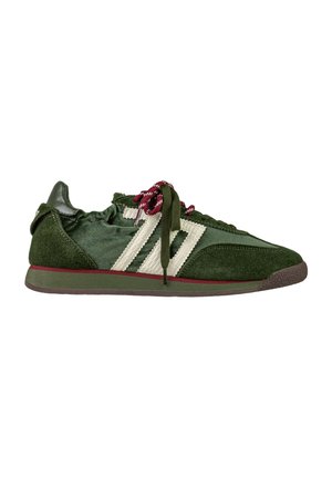 Sneaker verde a profilo basso con design di lacci bianchi, lacci a righe rosse e bianche, texture in suede e pelle e suola con accenti rossi.