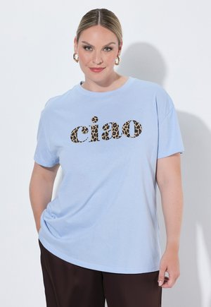 Vrouw met lichtbruin haar draagt gouden hoepel oorbellen en een lichtblauw T-shirt met "ciao" in luipaardprint letters.