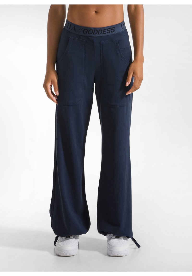 Marineblauwe wijde broek met een gestructureerde tailleband, voorzakken en strikjes bij de enkels. Gecombineerd met witte sneakers.